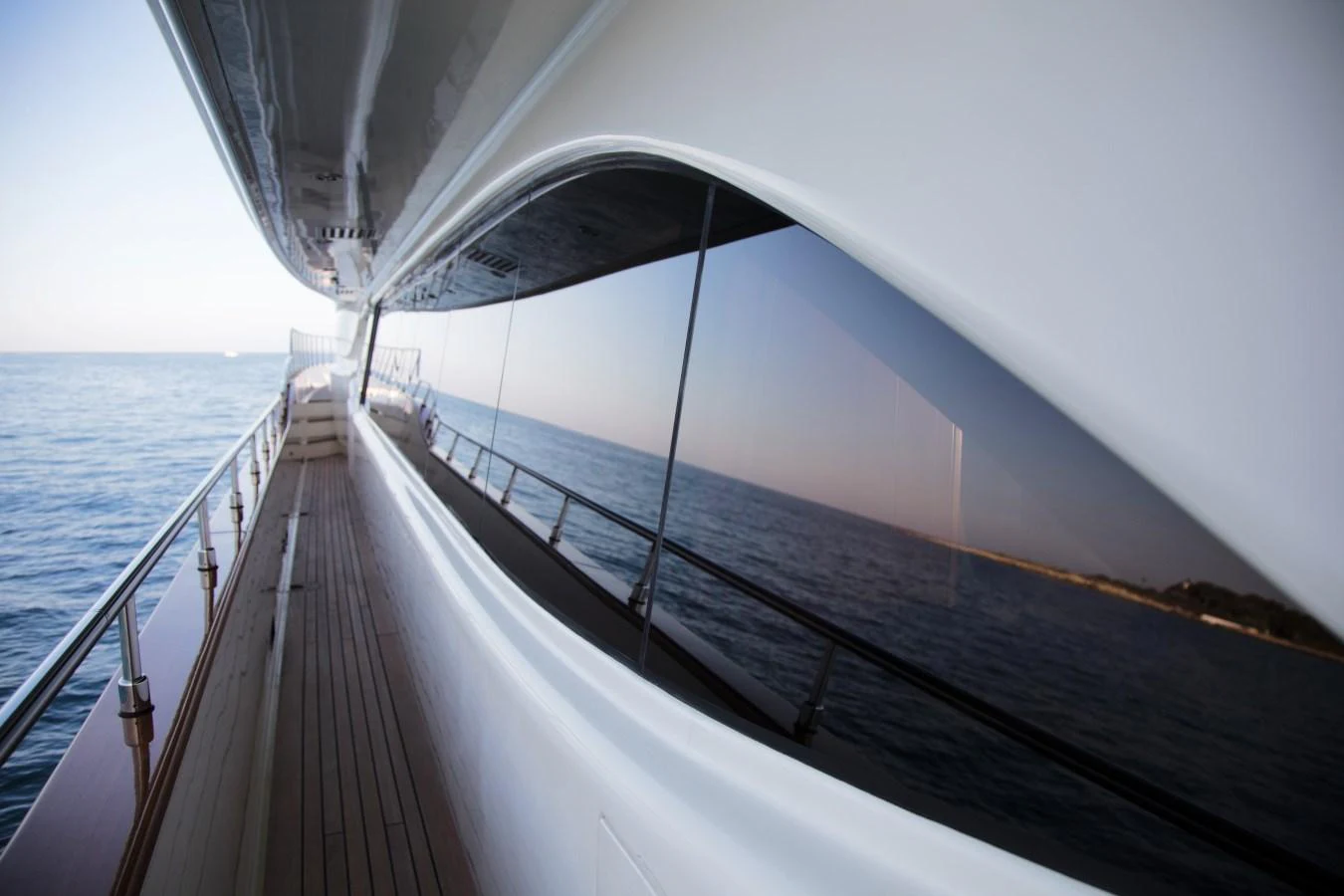 A sleek yacht exterior showcasing a reflective window and a wooden deck along the side. aboard SIMA Yacht for Sale