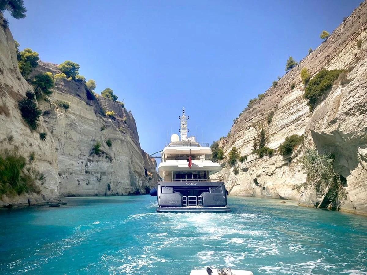 A luxurious yacht navigates through a scenic, narrow waterway flanked by towering cliffs. aboard SIMA Yacht for Sale