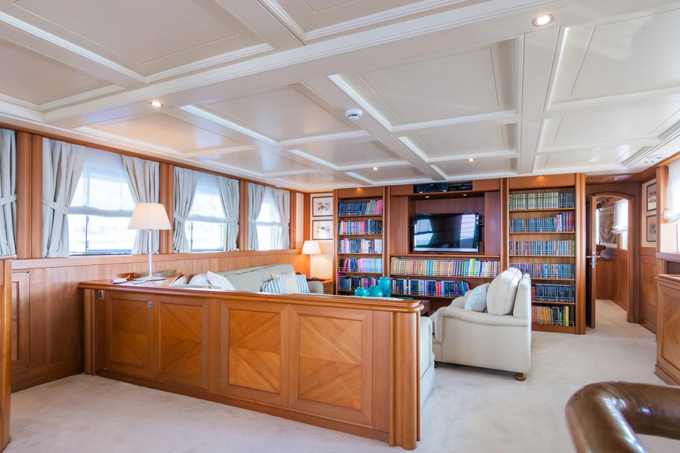 The salon features elegant wood paneling, plush seating, and a well-stocked bookshelf, creating a cozy and inviting atmosphere. aboard MESERRET Yacht for Sale