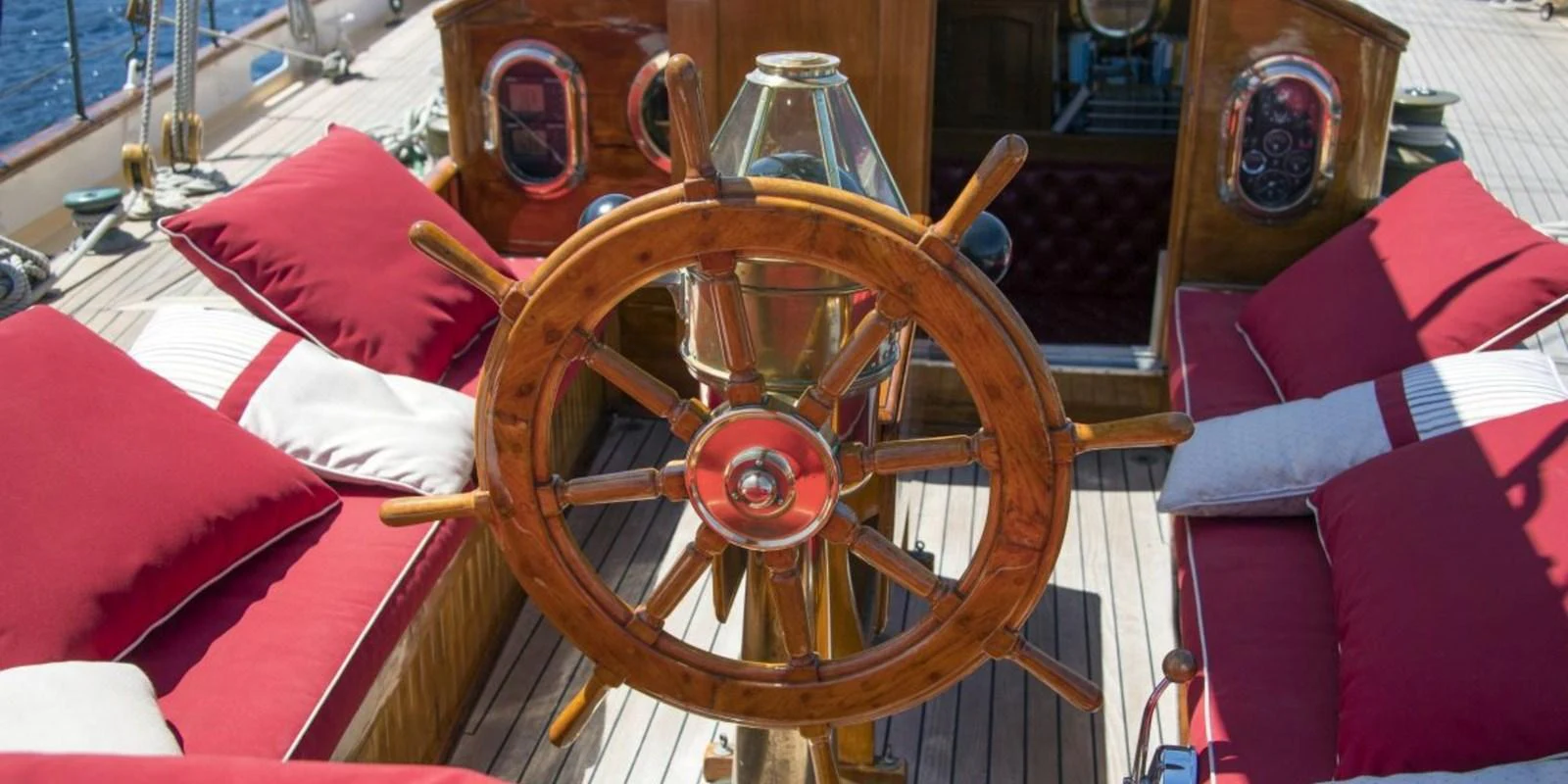 The yacht's helm features a classic wooden steering wheel surrounded by plush red and white seating. aboard PURITAN Yacht for Sale