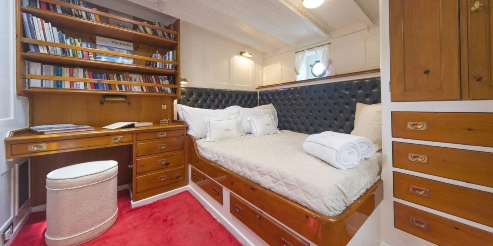 The stateroom features a cozy bed with elegant wood cabinetry and a well-stocked bookshelf. aboard PURITAN Yacht for Sale