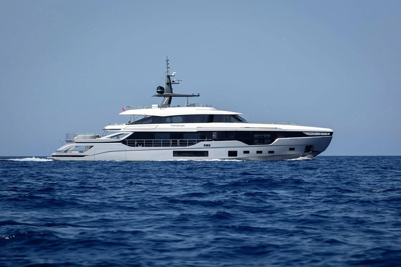 A sleek and modern yacht cruising on the open sea under a clear blue sky. aboard TAMANYA Yacht for Sale