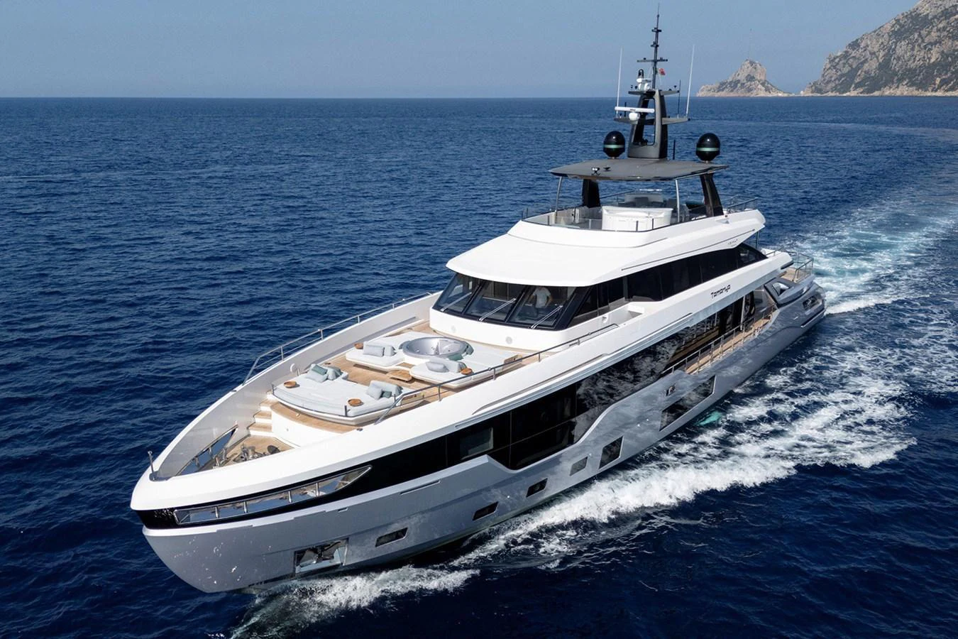 A sleek and modern yacht cruising through the open sea with a stunning coastal backdrop. aboard TAMANYA Yacht for Sale