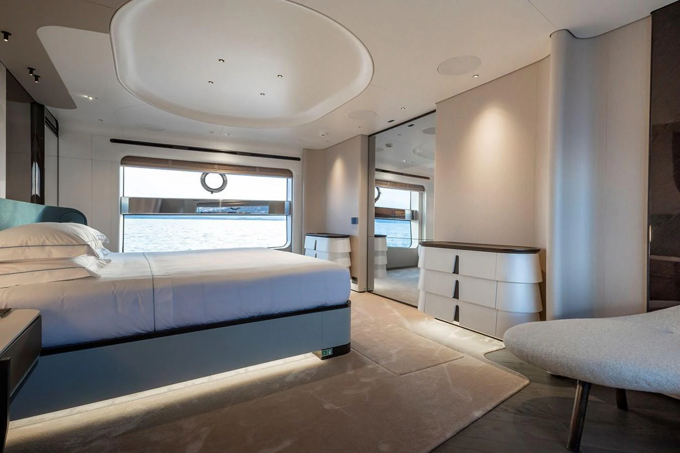 The stateroom features a luxurious bed with a serene view of the water through large windows. aboard TAMANYA Yacht for Sale