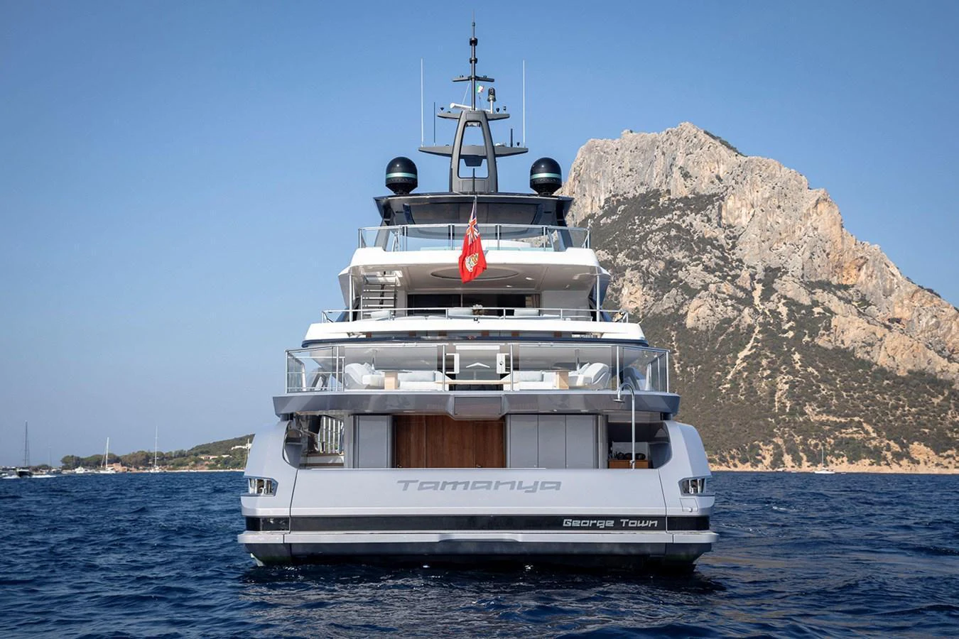 A luxurious yacht is anchored in calm waters with a scenic mountain backdrop. aboard TAMANYA Yacht for Sale