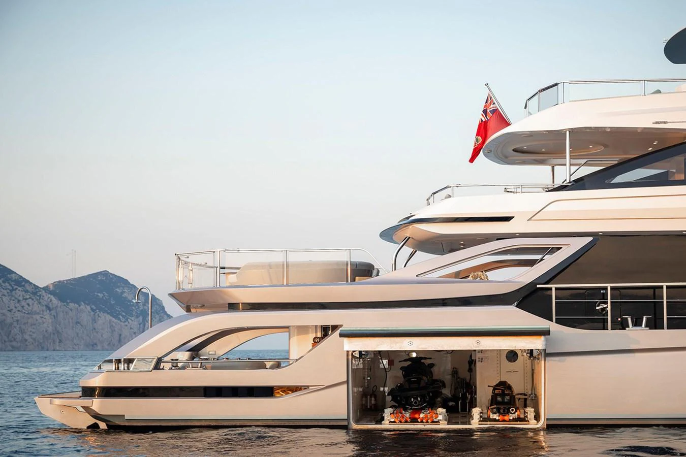 The yacht's elegant exterior showcases a garage with water toys against a serene coastal backdrop. aboard TAMANYA Yacht for Sale
