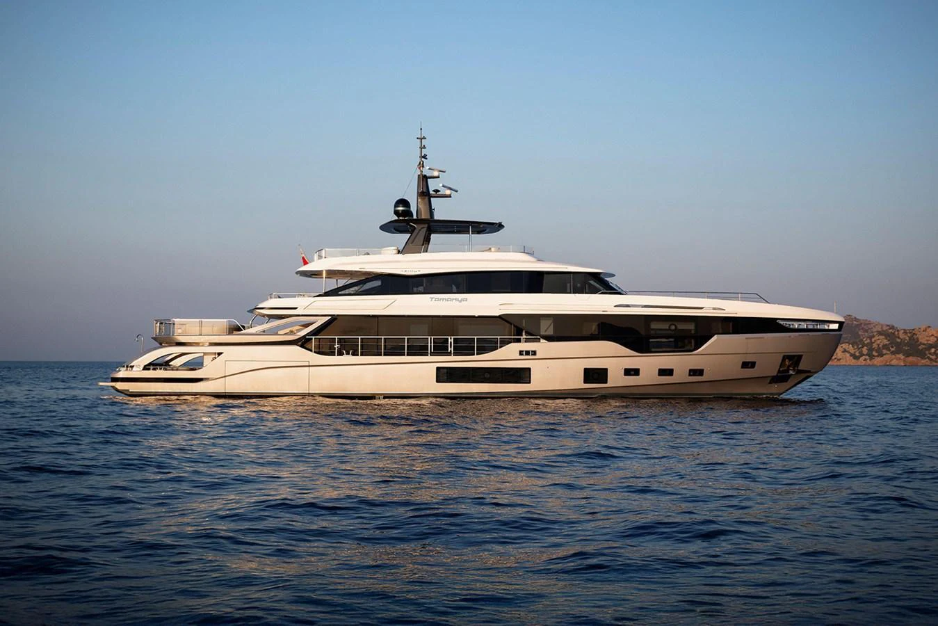 A sleek and modern yacht cruising on calm waters during sunset. aboard TAMANYA Yacht for Sale