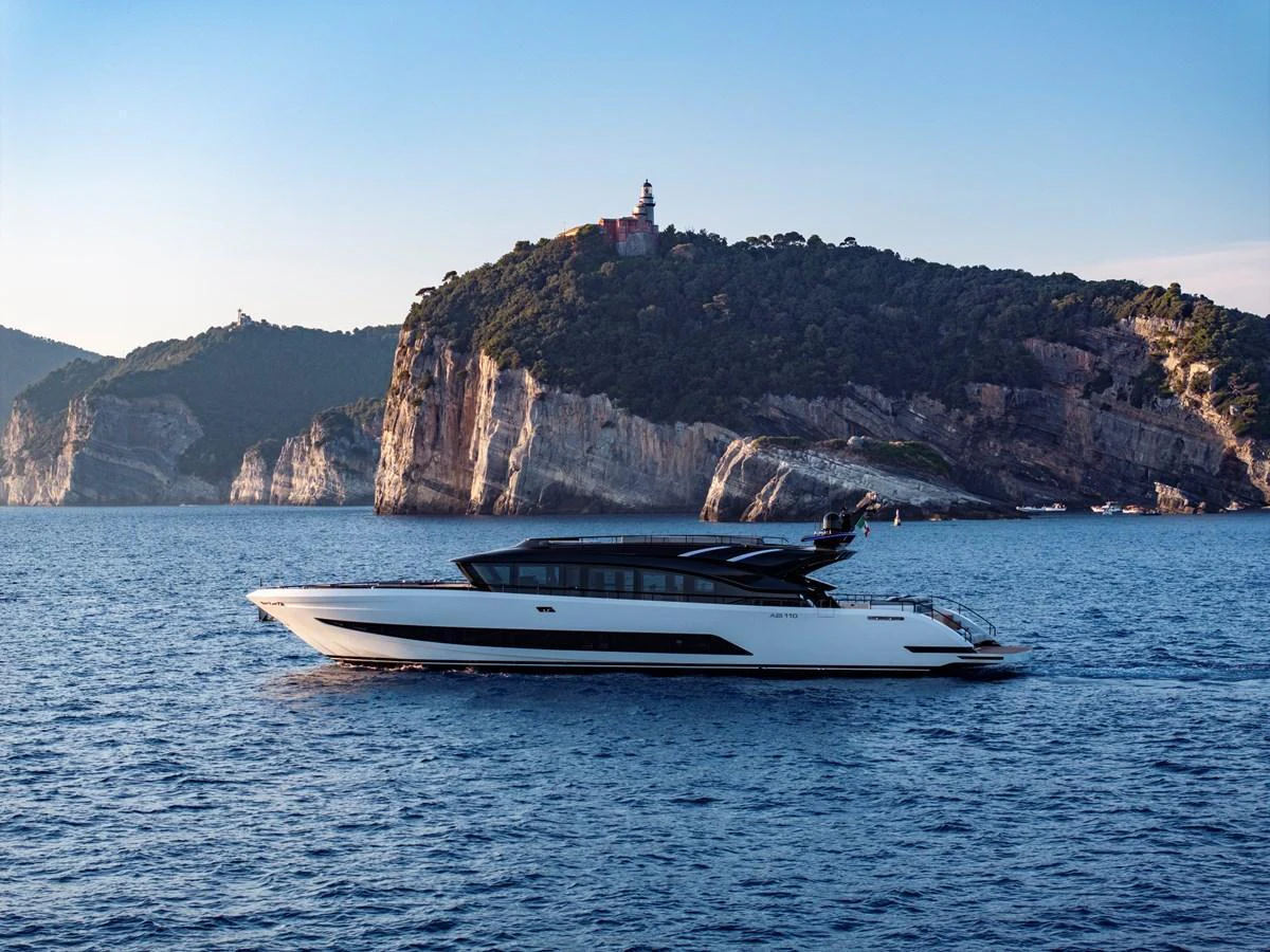 A sleek, modern yacht cruises along a scenic coastline with a lighthouse perched on a cliff in the background. aboard AB 110 Yacht for Sale