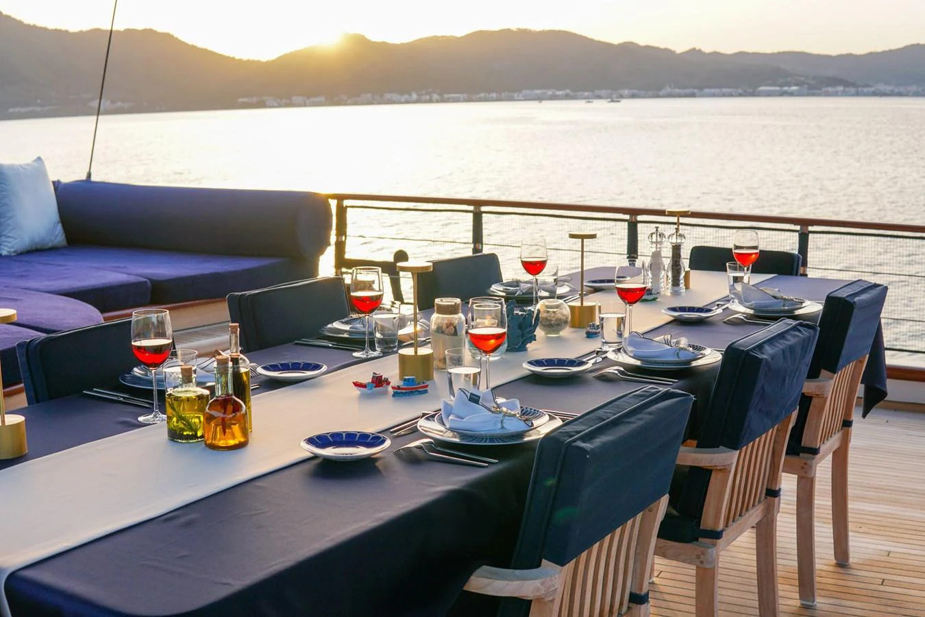 An elegant alfresco dining area set for a meal with a stunning view of the water and mountains at sunset. aboard VOYAGE Yacht for Sale