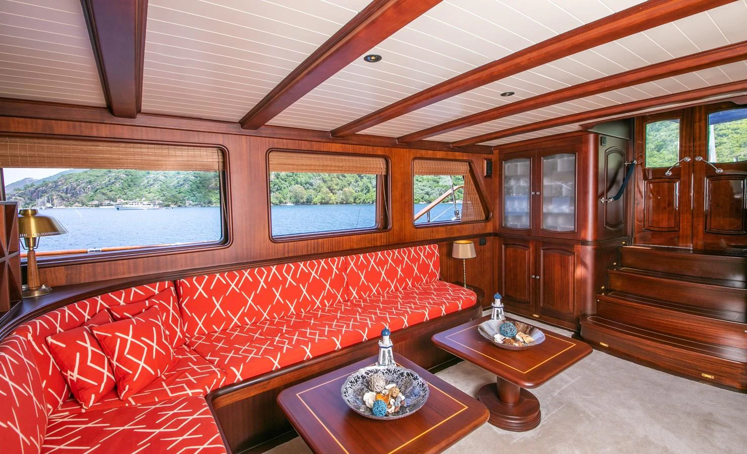 The salon features rich wood paneling and vibrant red seating with a view of the surrounding waters. aboard VOYAGE Yacht for Sale