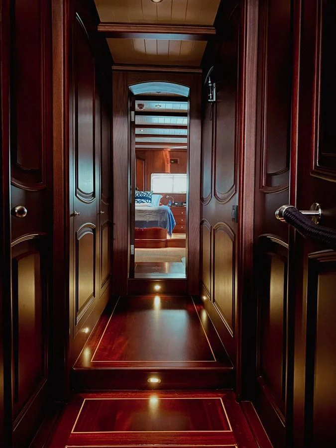 A luxurious hallway with rich wood paneling leads to a cozy stateroom. aboard VOYAGE Yacht for Sale