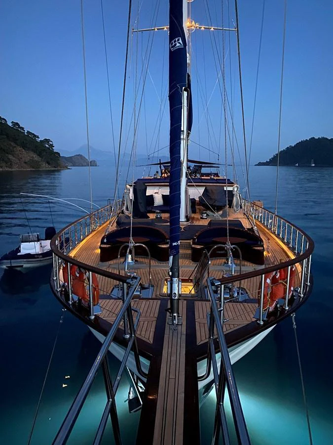 A stunning yacht is anchored in calm waters at dusk, with warm deck lighting creating a serene ambiance. aboard VOYAGE Yacht for Sale