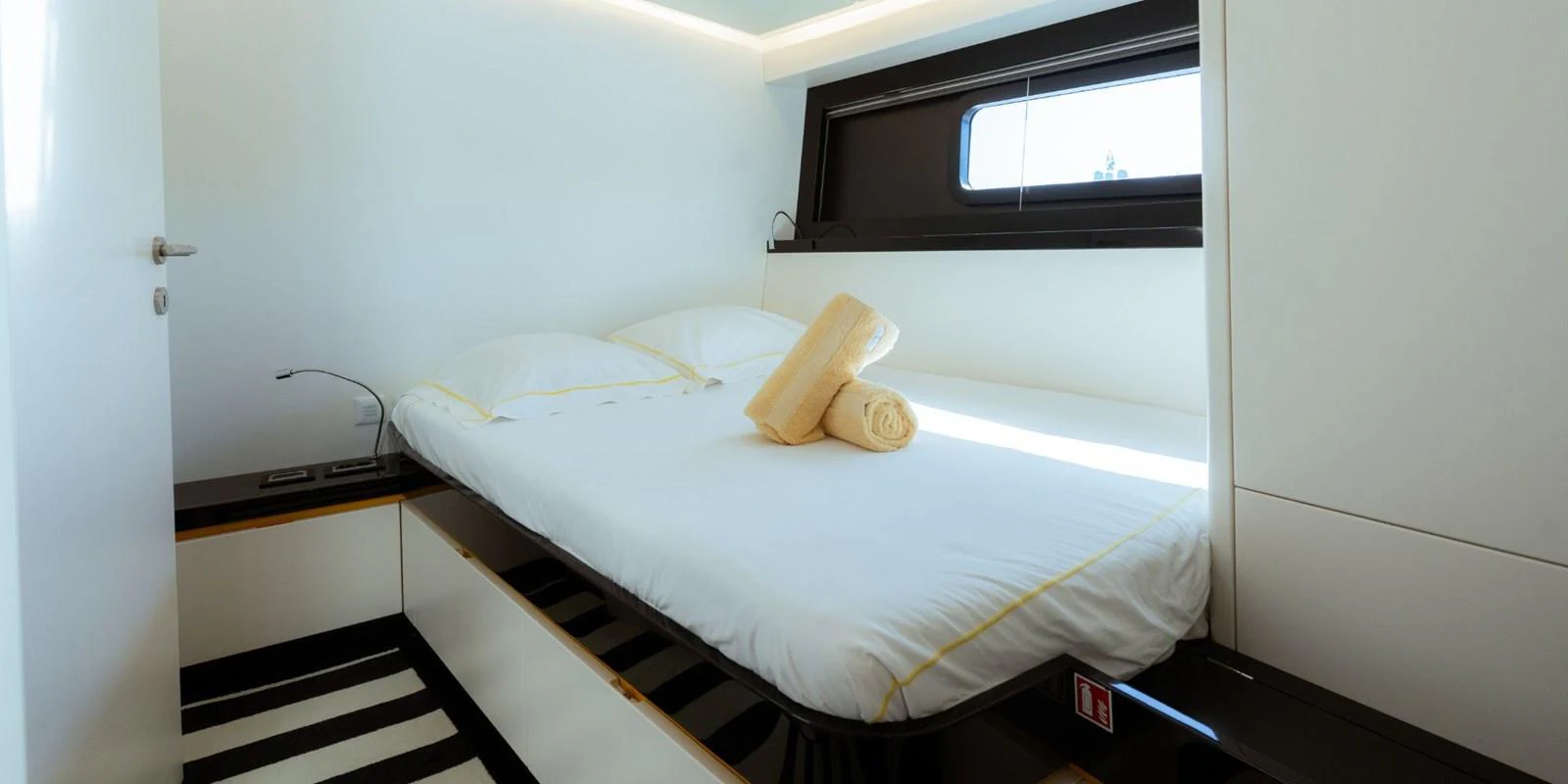 A cozy guest stateroom featuring a comfortable bed with neatly arranged towels and modern decor. aboard NOMAD IV Yacht for Sale
