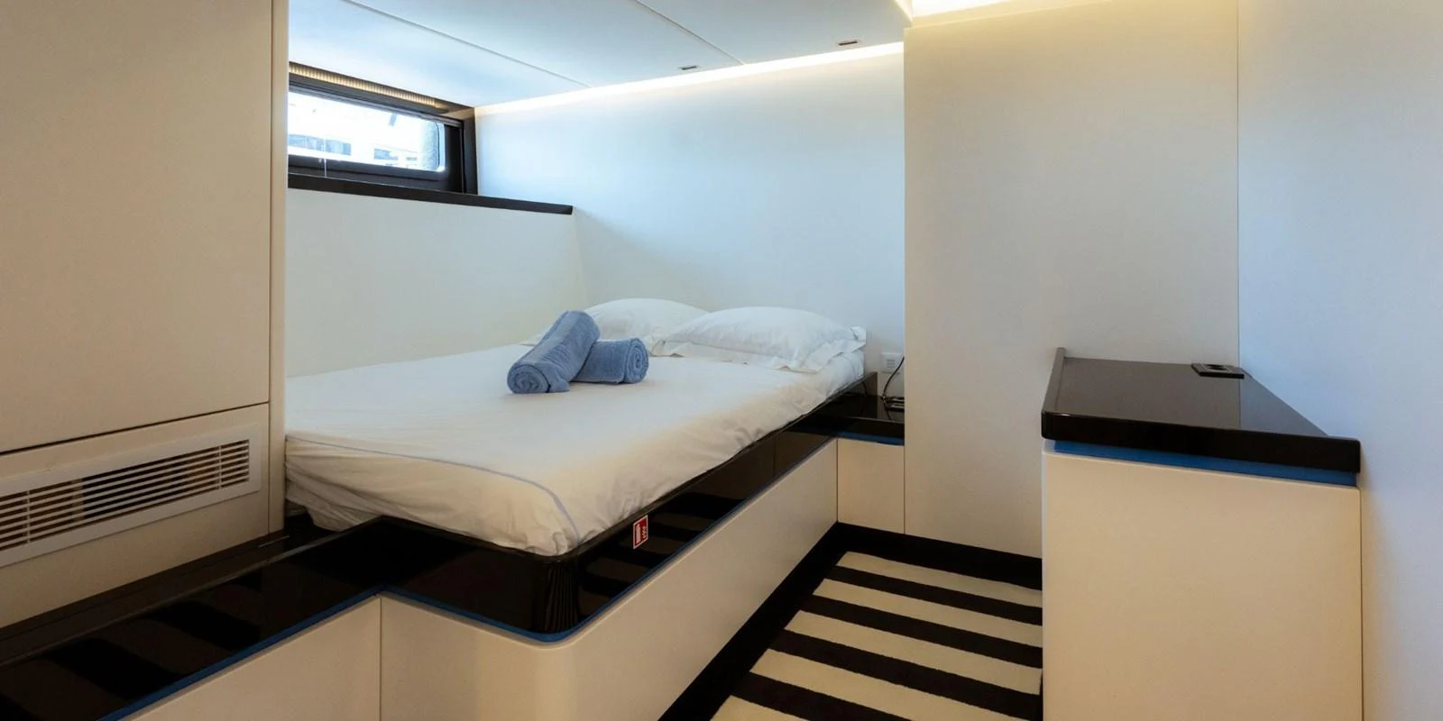 A modern guest stateroom featuring a comfortable bed with neatly folded towels and minimalist decor. aboard NOMAD IV Yacht for Sale