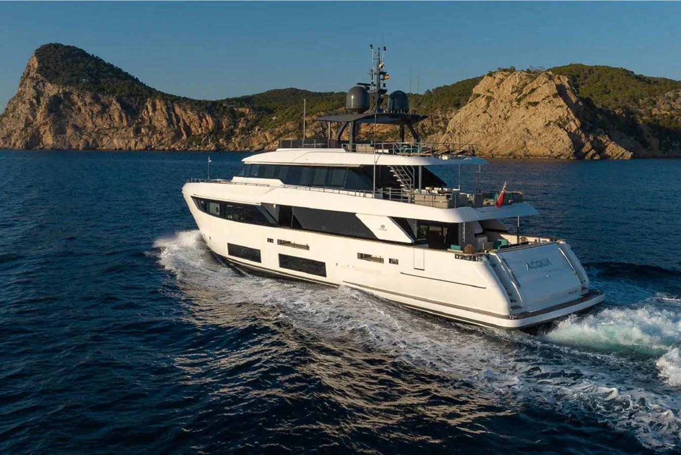 A sleek and modern yacht cruising in clear blue waters with a scenic rocky coastline in the background. aboard ON Yacht for Sale
