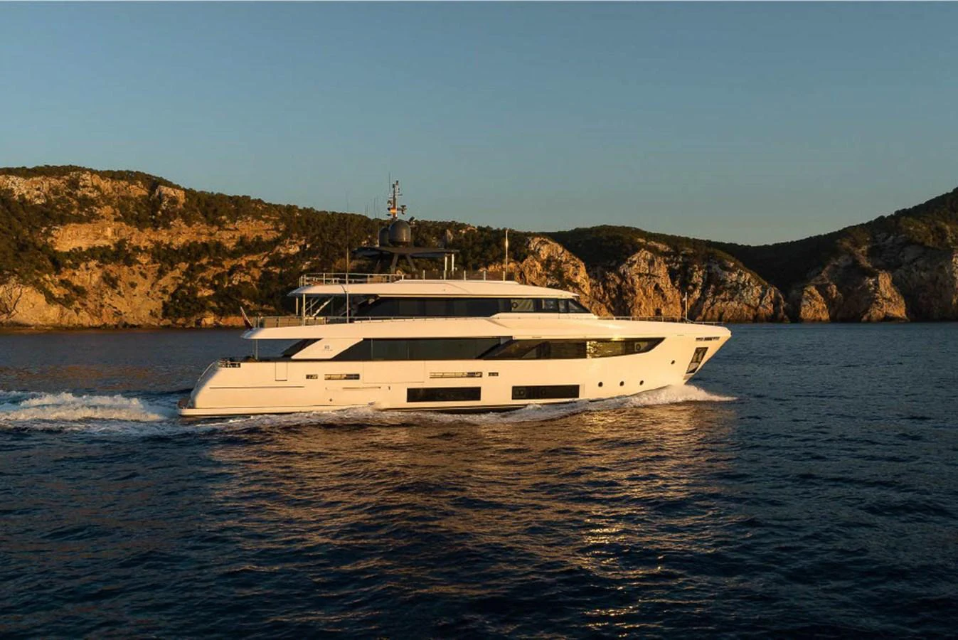 A sleek and modern yacht cruises along the coastline at sunset. aboard ON Yacht for Sale