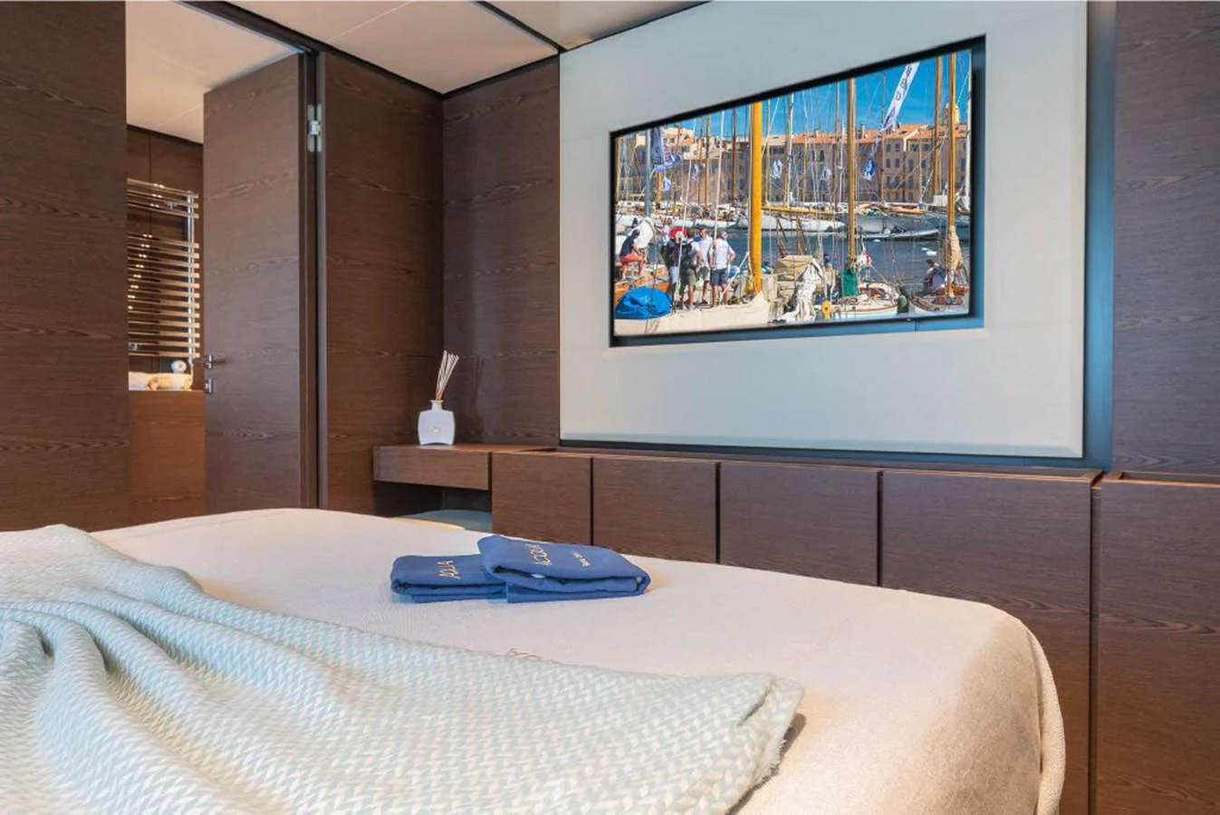 A cozy stateroom featuring a large bed, wooden cabinetry, and a wall-mounted TV displaying a marina scene. aboard ON Yacht for Sale