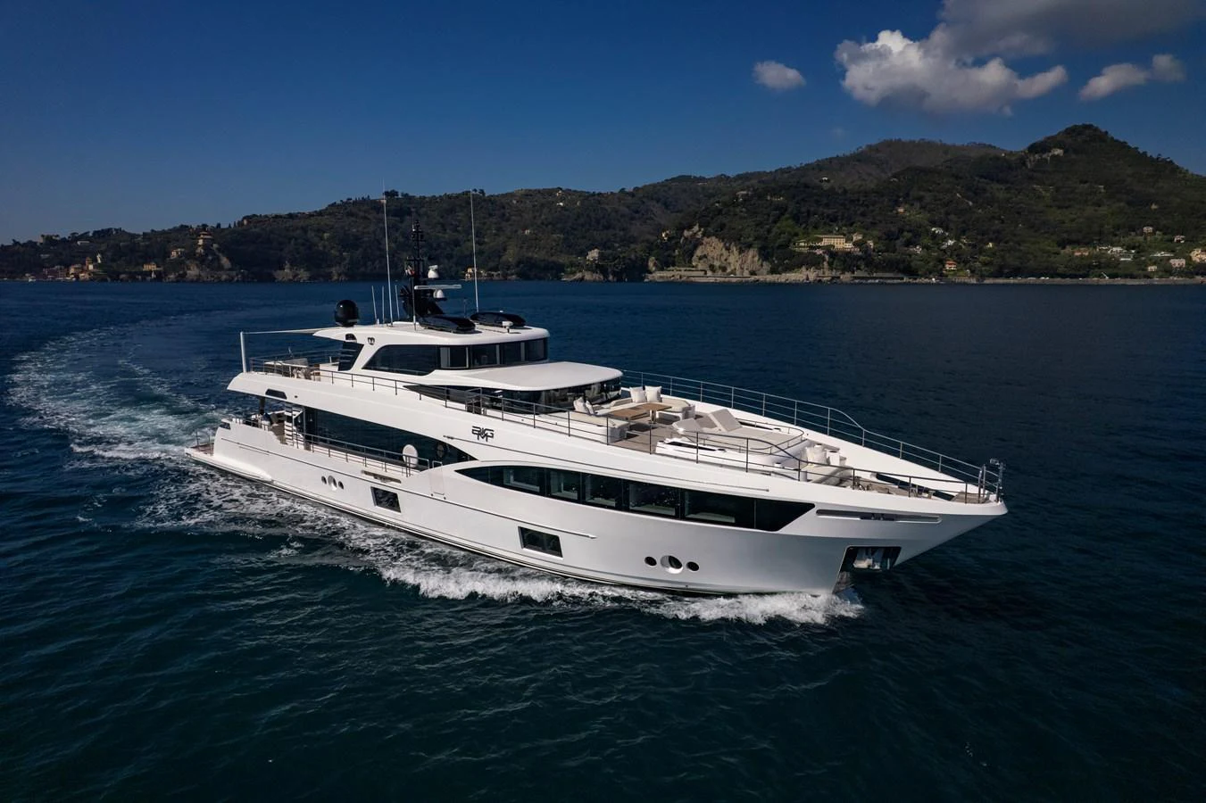 A sleek and modern yacht cruises through calm waters with a scenic coastline in the background. aboard BIG M Yacht for Sale