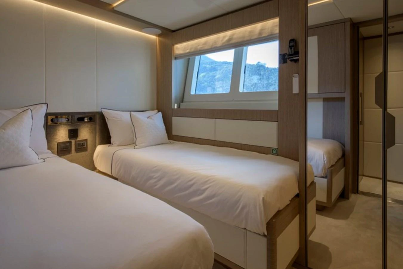 The guest stateroom features twin beds and a serene atmosphere with natural light from the large window. aboard BIG M Yacht for Sale