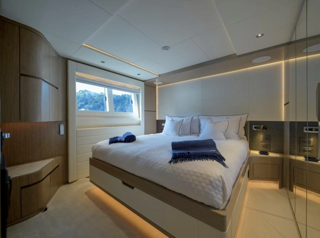 The stateroom features a luxurious bed with elegant linens and ample natural light from large windows. aboard BIG M Yacht for Sale