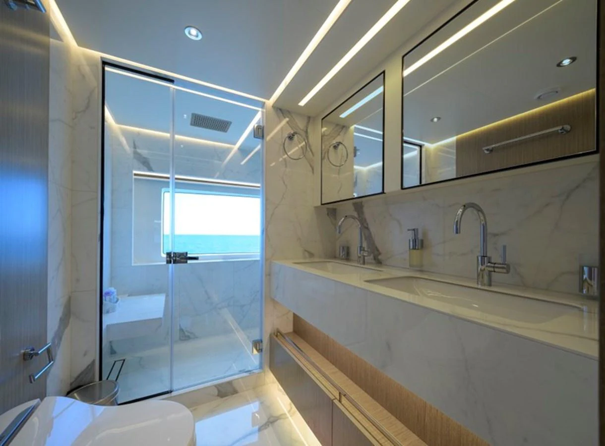 A luxurious yacht bathroom featuring dual sinks, a large mirror, and a spacious shower area with a view of the sea. aboard BIG M Yacht for Sale