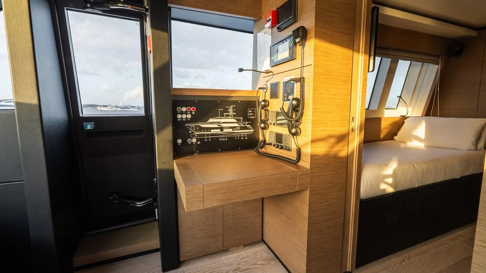 The image showcases a cozy cabin with a control panel and a comfortable bed, bathed in warm natural light. aboard QUEEN J III Yacht for Sale