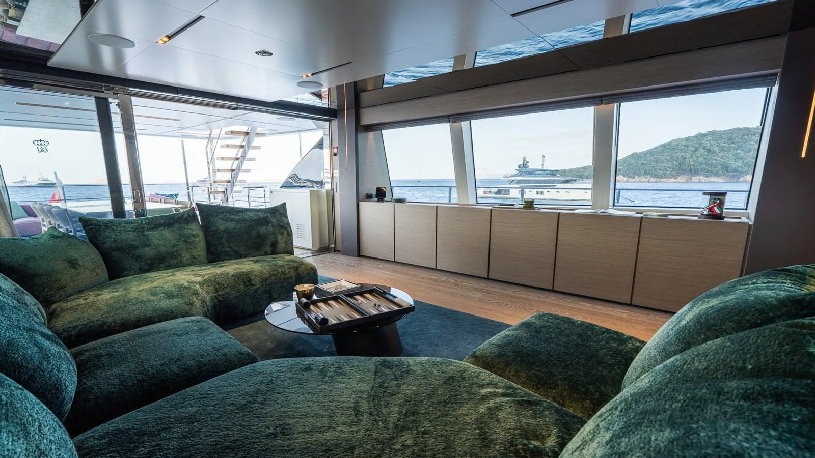 The salon features plush green seating with panoramic windows offering stunning sea views. aboard QUEEN J III Yacht for Sale