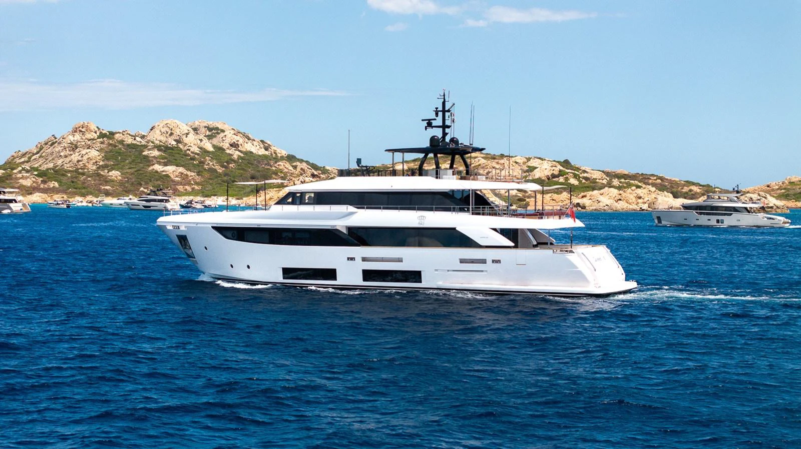 A sleek and modern yacht cruising through clear blue waters with a scenic rocky coastline in the background. aboard QUEEN J III Yacht for Sale