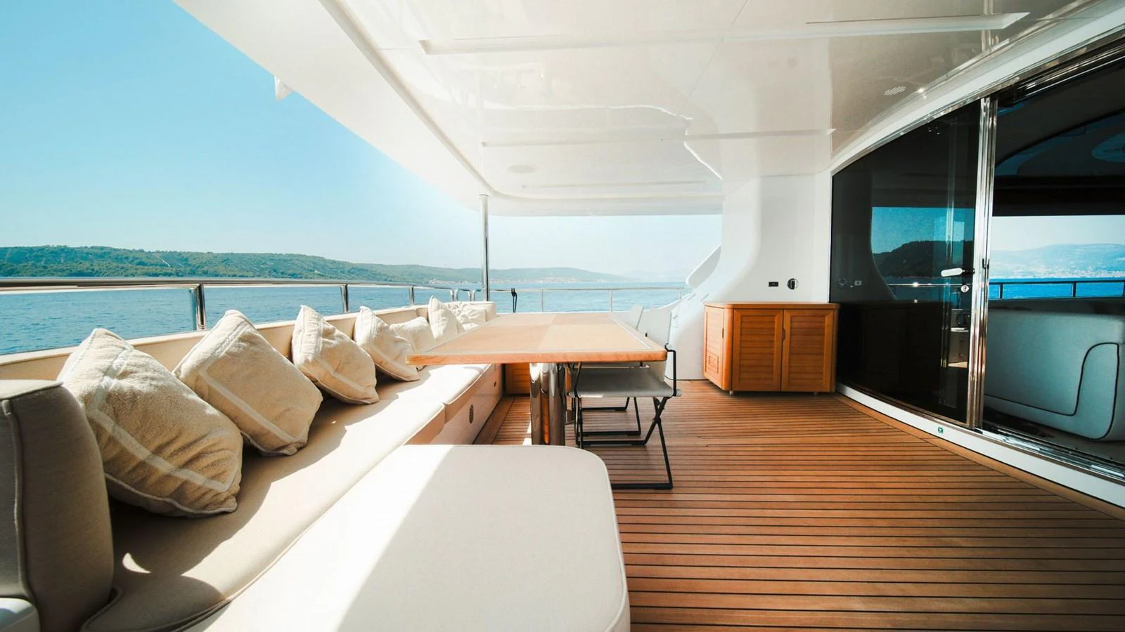 The aft deck features a spacious seating area with plush cushions and a wooden table, perfect for outdoor relaxation and dining. aboard AFINA Yacht for Sale