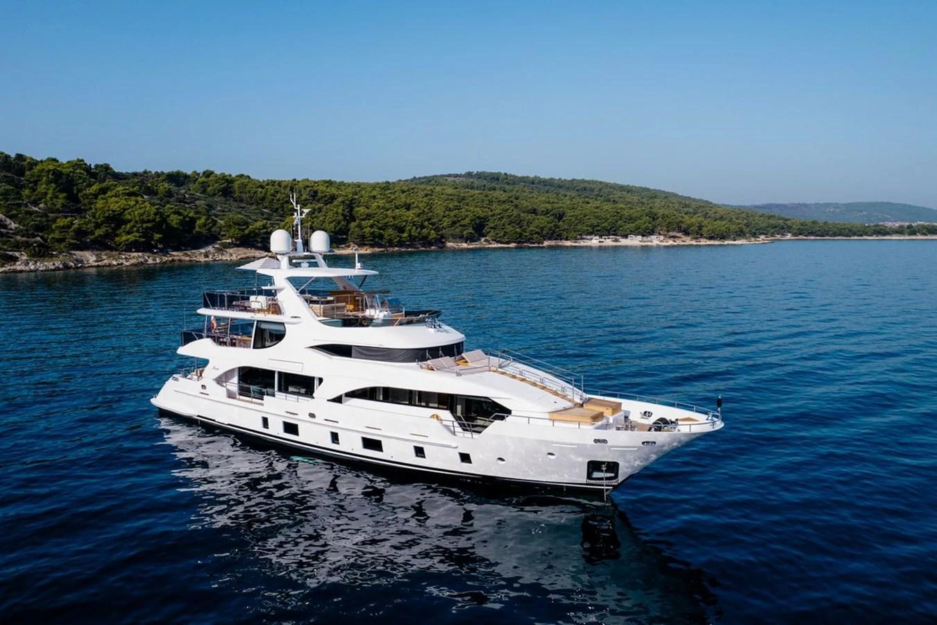 A luxurious yacht cruises through calm blue waters with a scenic coastline in the background. aboard AFINA Yacht for Sale