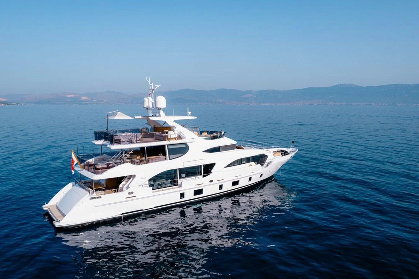 A pristine white yacht glides gracefully on calm waters under a clear blue sky. aboard AFINA Yacht for Sale