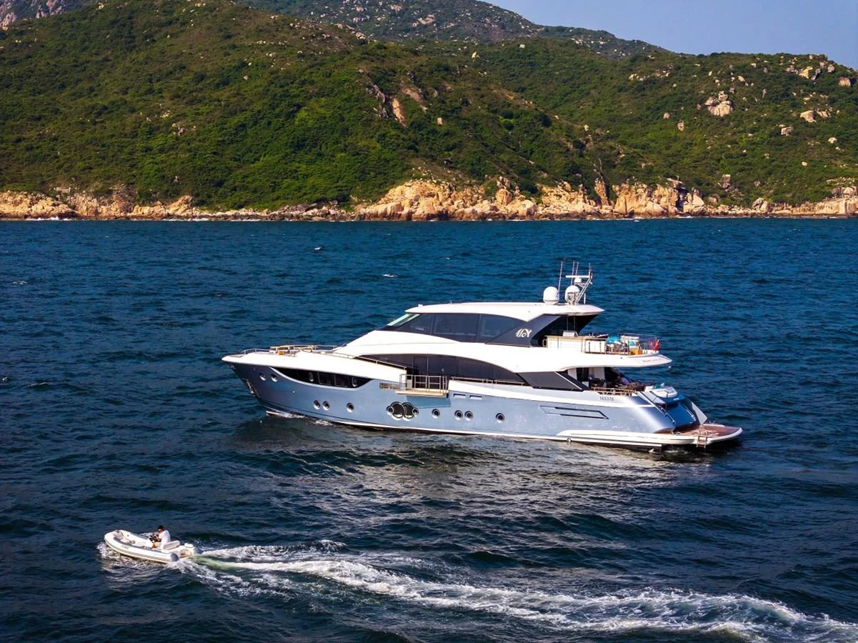 A sleek yacht cruises along a scenic coastline with a tender boat in tow. aboard MIRAE Yacht for Sale