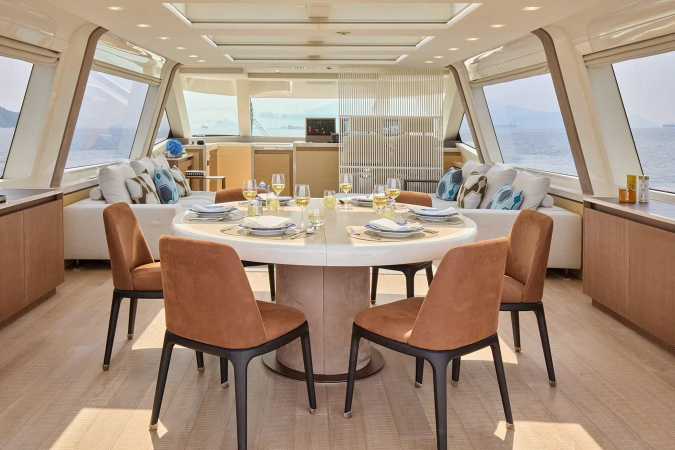The yacht's dining area features a stylish round table surrounded by comfortable chairs, with panoramic windows offering stunning sea views. aboard MIRAE Yacht for Sale