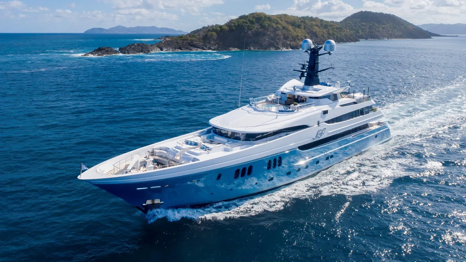 A sleek and luxurious yacht cruising through clear blue waters with scenic islands in the background. aboard SCOTT FREE Yacht for Sale