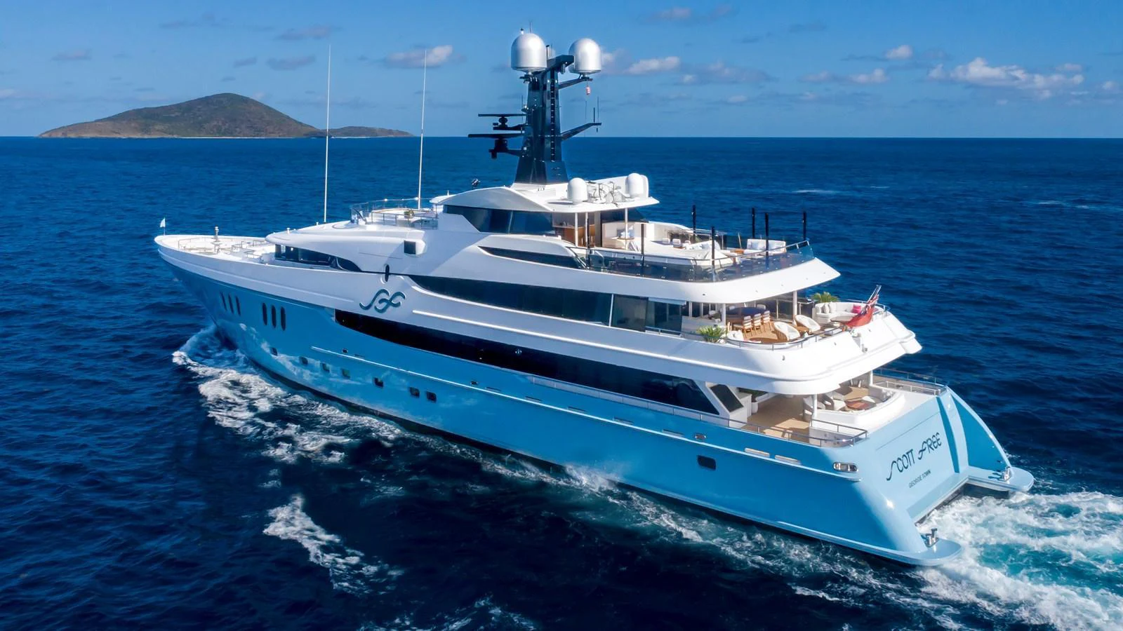 A luxurious yacht cruising through clear blue waters with an island in the background. aboard SCOTT FREE Yacht for Sale
