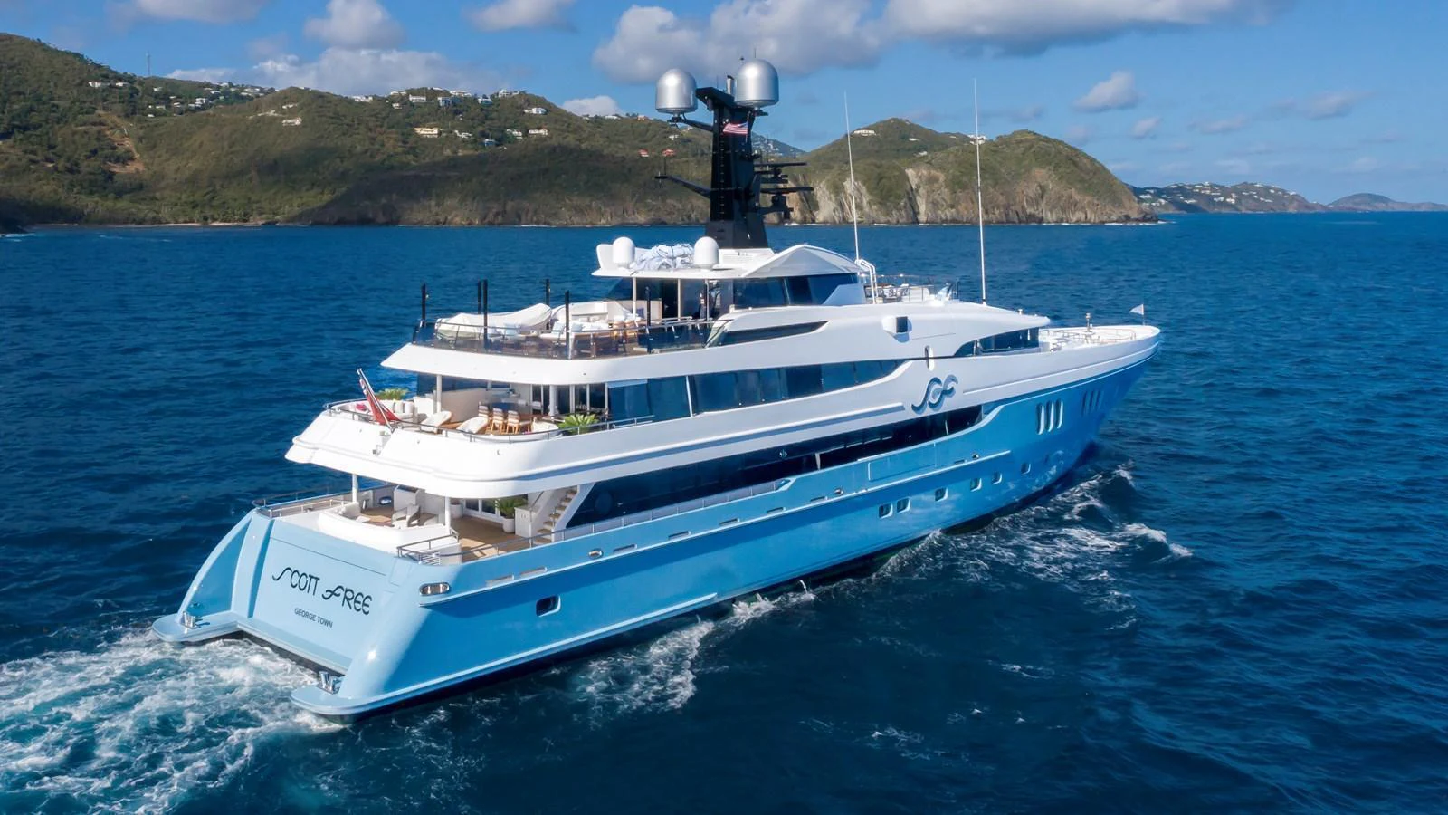 A luxurious yacht cruises through pristine blue waters with scenic hills in the background. aboard SCOTT FREE Yacht for Sale