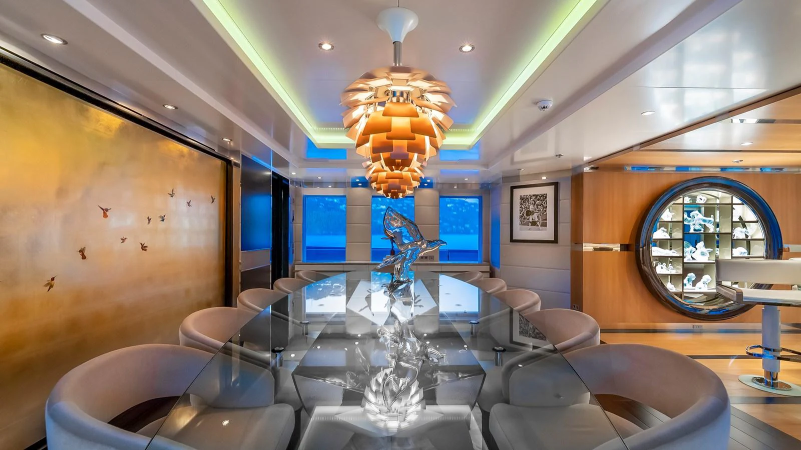 The yacht's dining area features a modern design with a striking chandelier and a reflective glass table. aboard SCOTT FREE Yacht for Sale