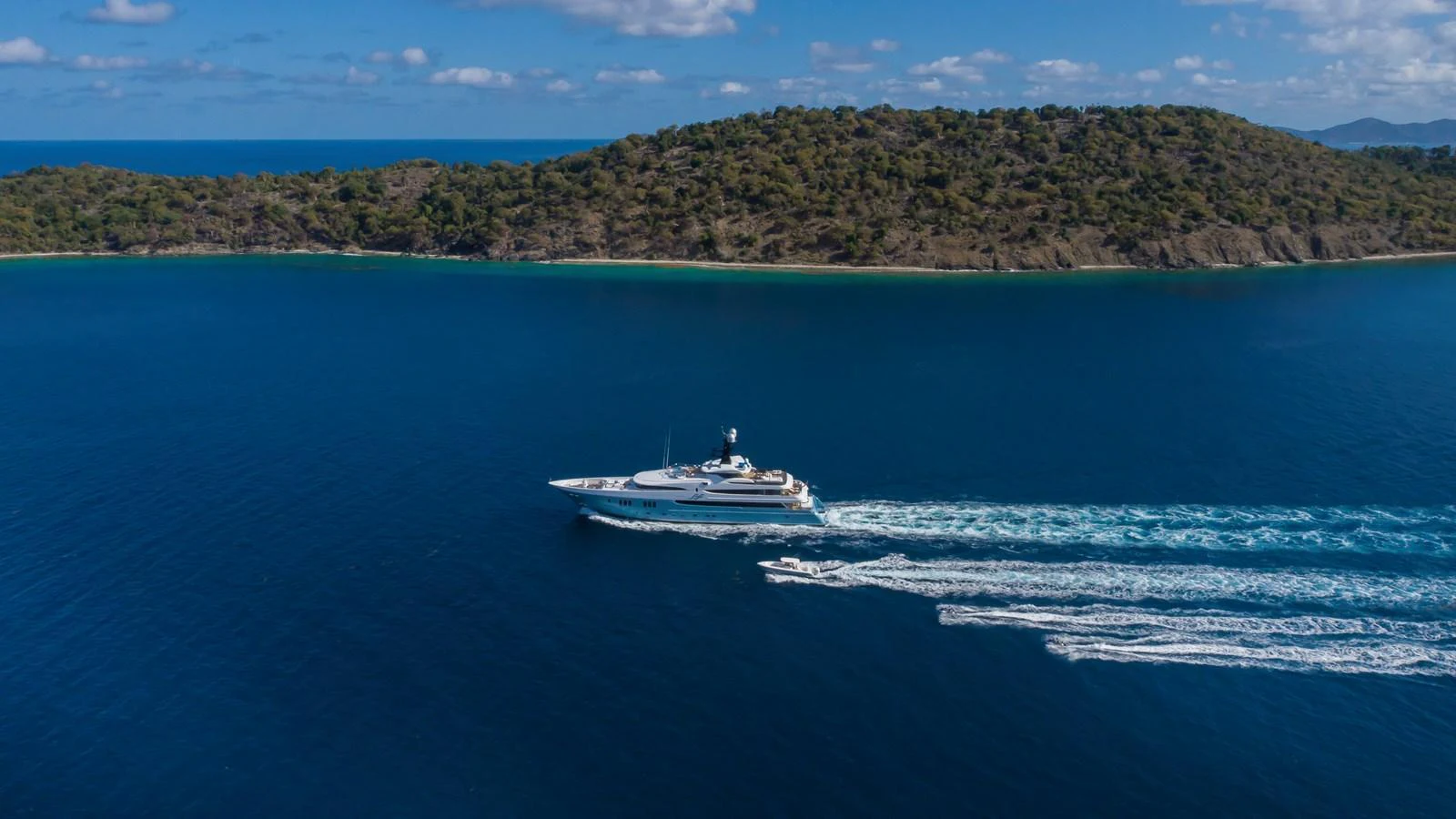 A sleek yacht cruises through pristine blue waters with a scenic island backdrop. aboard SCOTT FREE Yacht for Sale