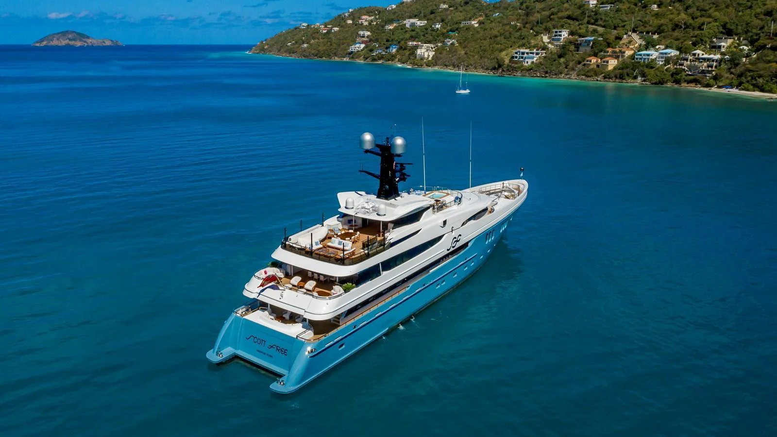 A luxurious yacht cruises through pristine blue waters with a scenic coastline in the background. aboard SCOTT FREE Yacht for Sale