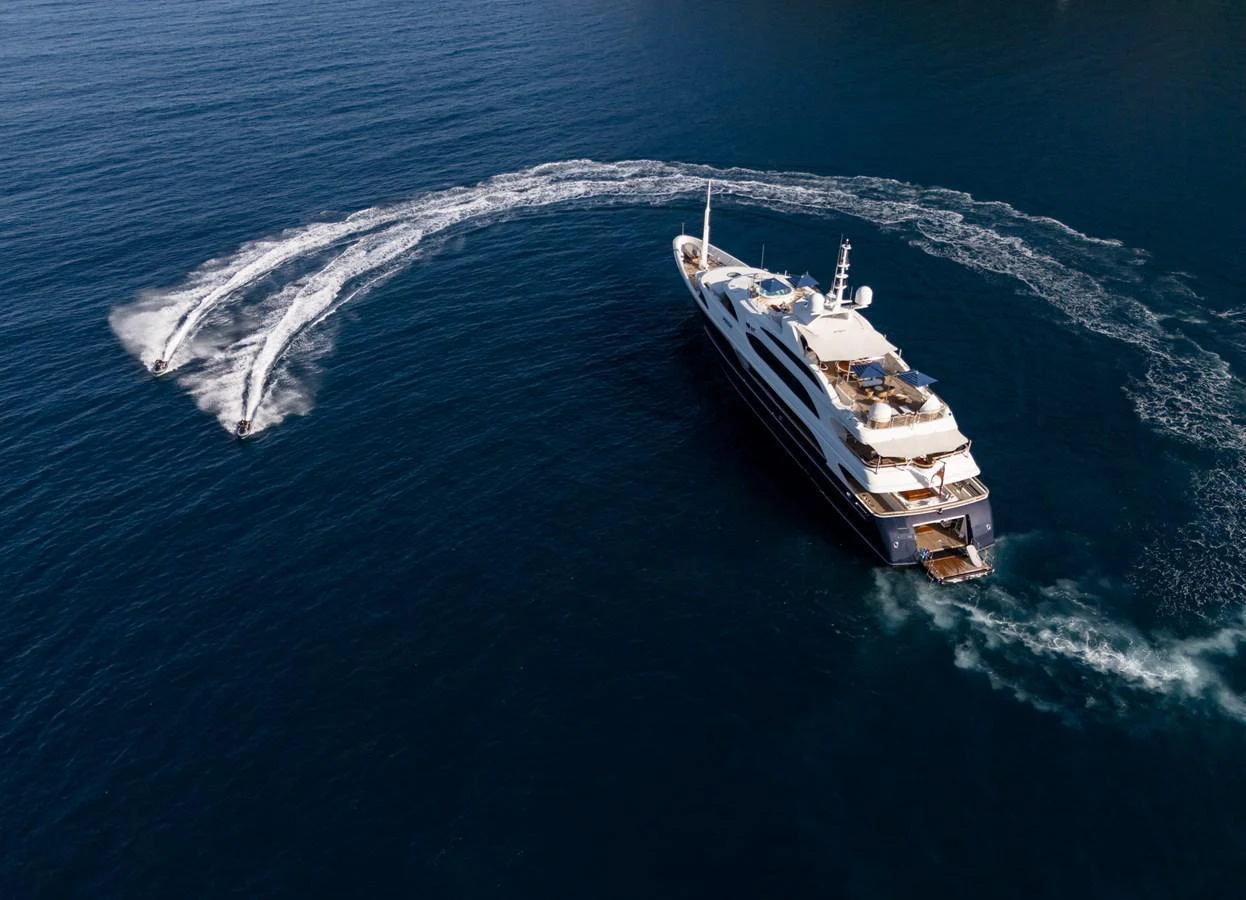 A luxurious yacht cruises through the open sea, accompanied by two jet skis creating dynamic water trails. aboard VISION Yacht for Sale