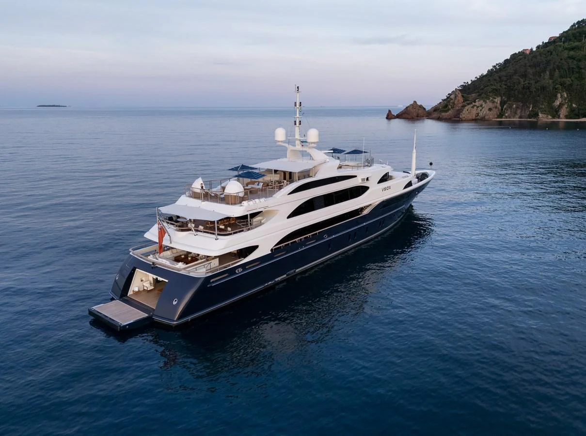 A luxurious yacht glides gracefully on calm waters near a scenic coastline. aboard VISION Yacht for Sale