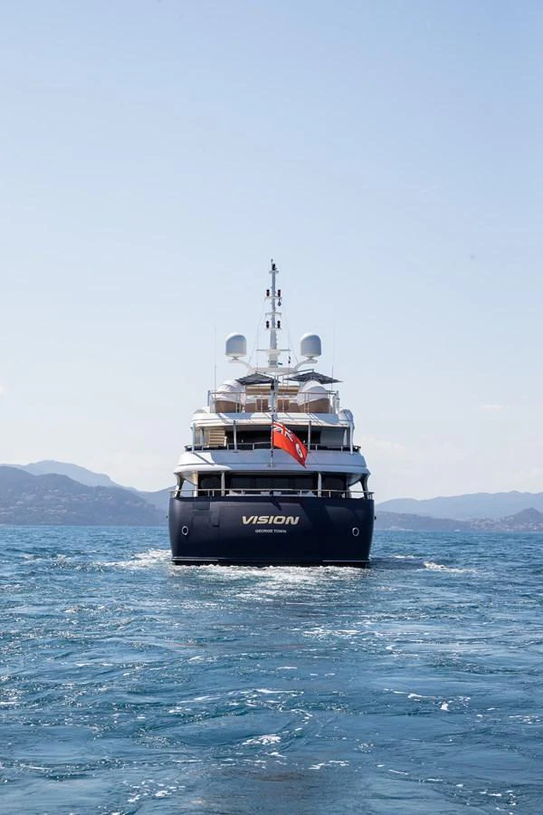 A luxurious yacht sails on the open sea with a scenic mountainous backdrop. aboard VISION Yacht for Sale