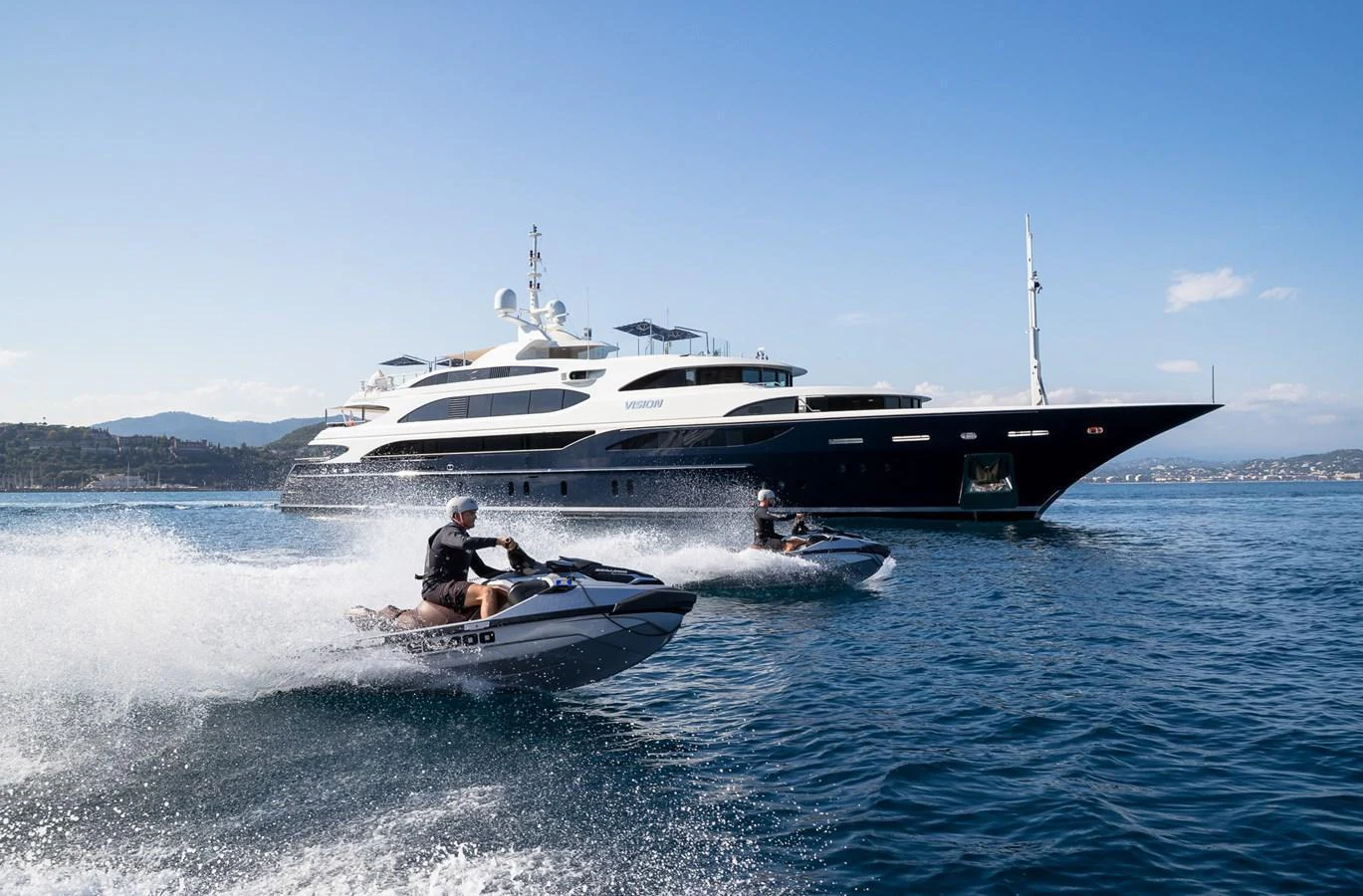 A luxurious yacht cruises on the water with two jet skis speeding alongside. aboard VISION Yacht for Sale