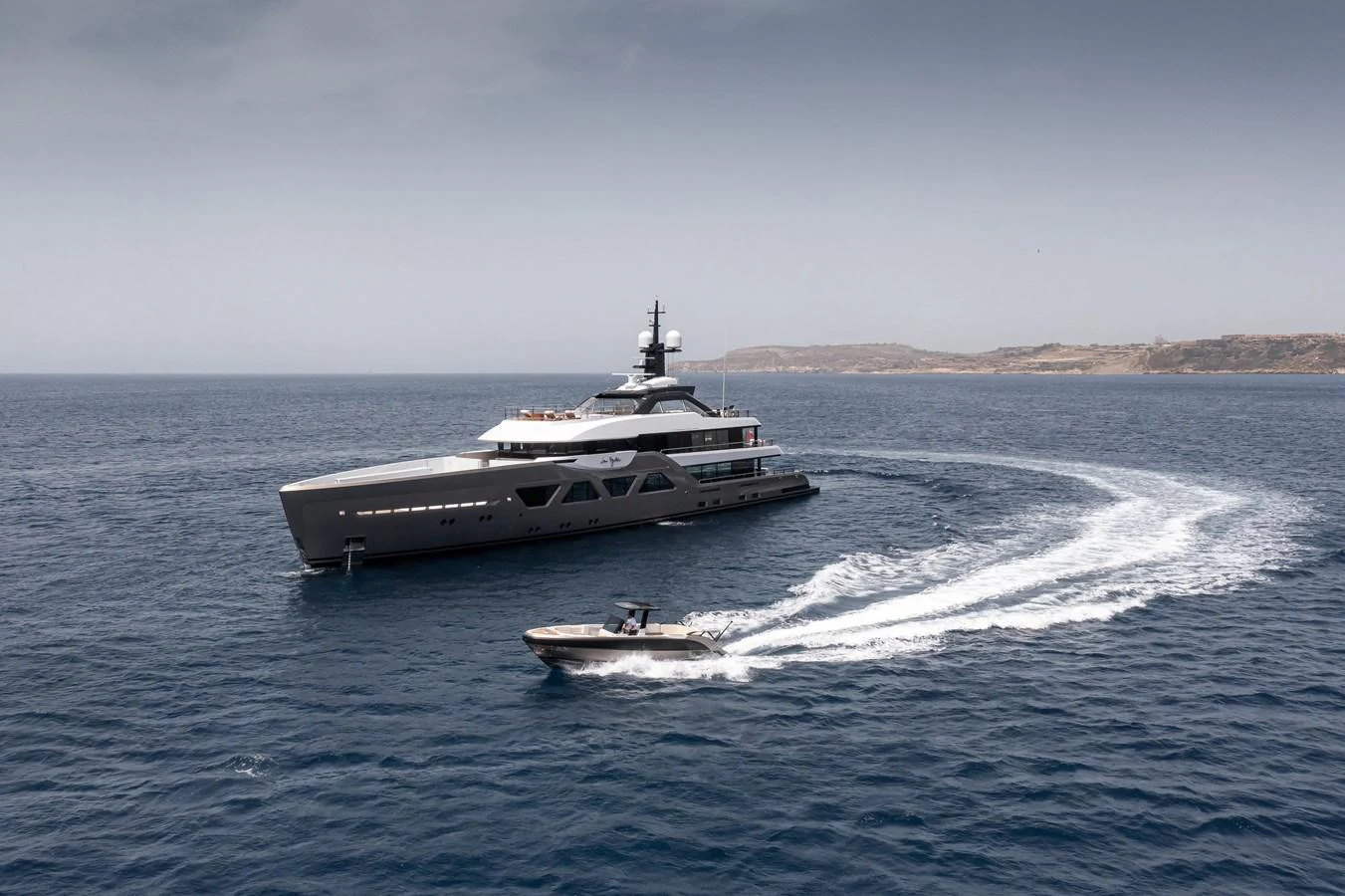 A sleek, modern yacht cruising on open waters with a tender boat speeding nearby. aboard AMELS 60 Yacht for Sale