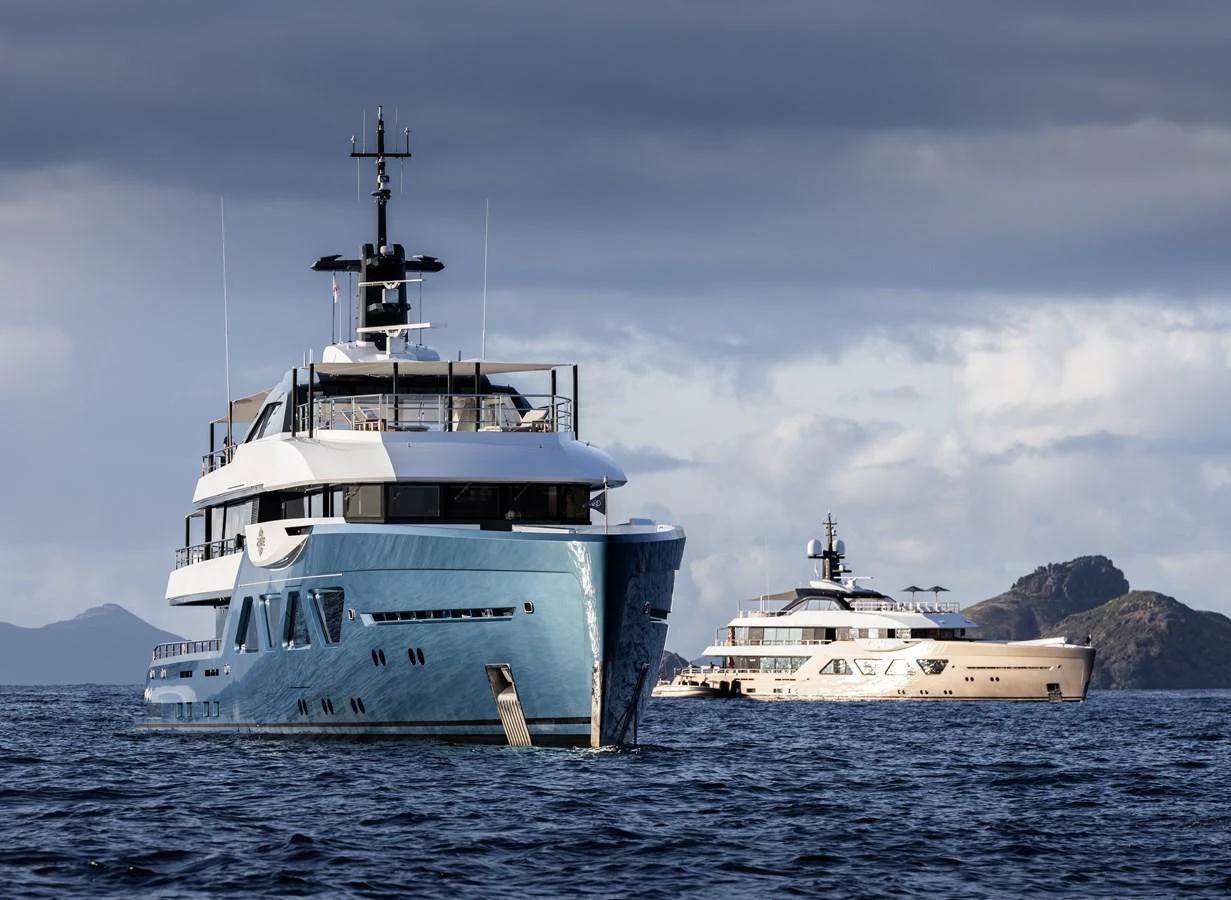 Two luxurious yachts are anchored in a serene, open water setting with a dramatic sky overhead. aboard AMELS 60 Yacht for Sale