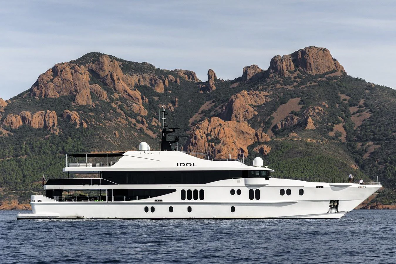 A sleek and modern yacht cruises along a scenic coastline with rugged hills in the background. aboard IDOL Yacht for Sale
