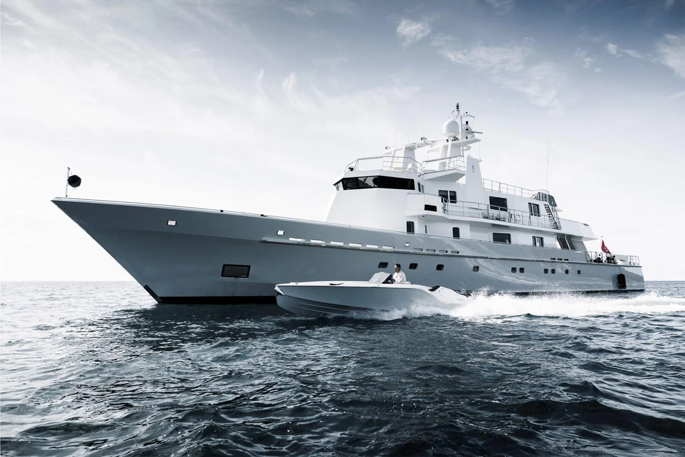 A sleek yacht glides through the water with a tender alongside, showcasing its impressive size and modern design. aboard RONIN Yacht for Sale