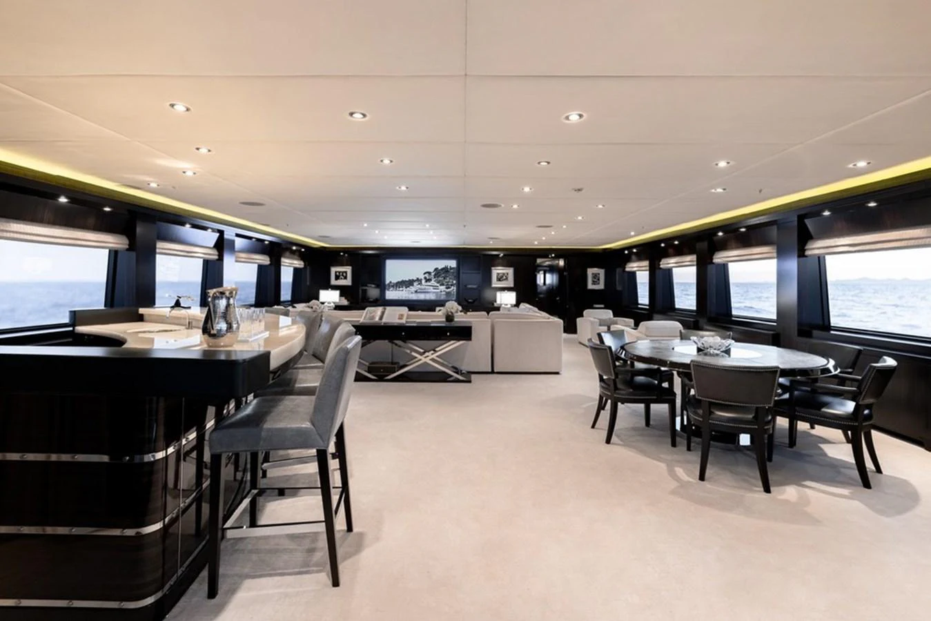 The spacious salon features elegant seating areas, a dining table, and a bar, all with panoramic views through large windows. aboard CARPE DIEM Yacht for Sale