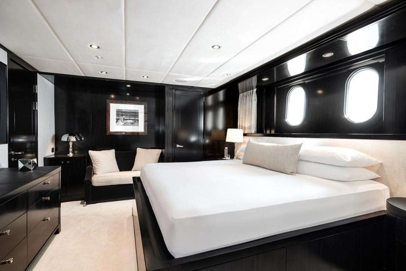 A luxurious stateroom featuring a large bed, elegant dark wood finishes, and ample natural light from porthole windows. aboard CARPE DIEM Yacht for Sale