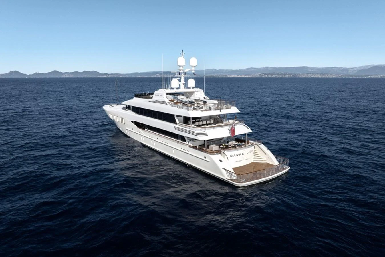 A sleek and luxurious yacht cruising on calm waters with a scenic coastline in the background. aboard CARPE DIEM Yacht for Sale